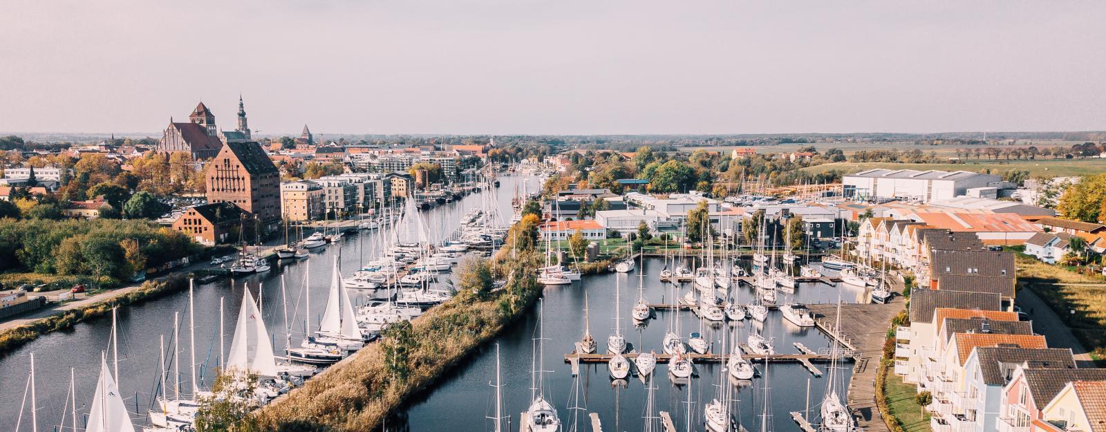 Greifswald: Blick über den Fluss Ryck mit zahlreichen Segelbooten im Hintergrund Speichergebäude aus Backstein
