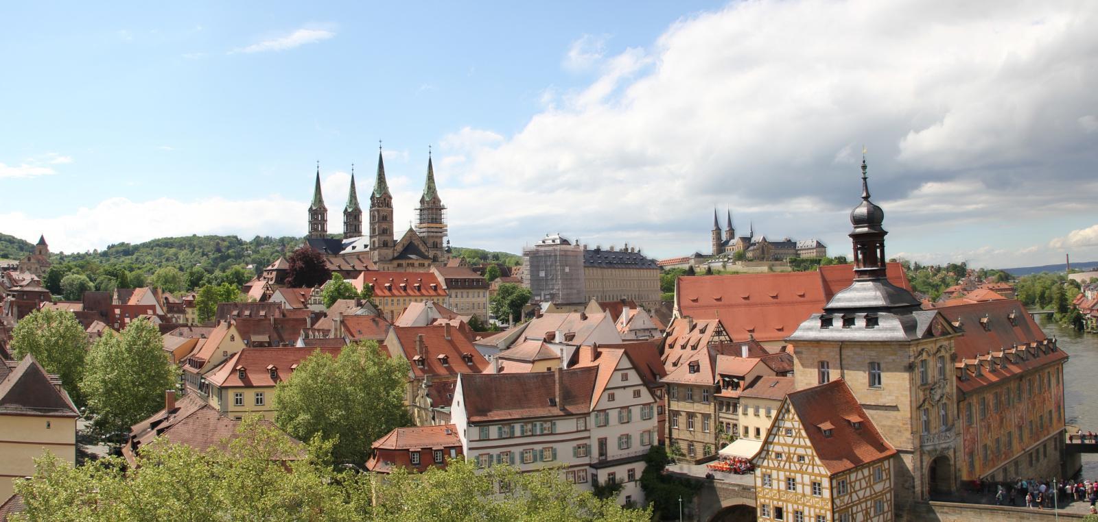 Blick über die Stadt, die sich in grüne Hügel einfügt. Einige der historischen Gebäude haben Türme oder fallen durch ihr Fachwerk auf.