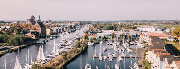 Greifswald: Blick über den Fluss Ryck mit zahlreichen Segelbooten im Hintergrund Speichergebäude aus Backstein