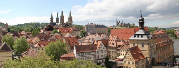 Blick über die Stadt, die sich in grüne Hügel einfügt. Einige der historischen Gebäude haben Türme oder fallen durch ihr Fachwerk auf.