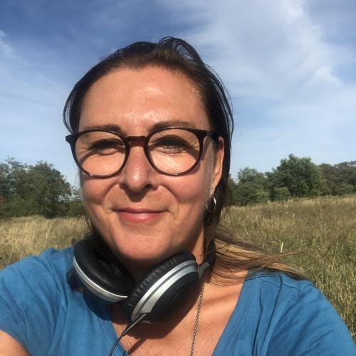 Foto von Elle Langer, einer weißen Frau mit Brille und braunen Haaren, draußen vor einem blauen Himmel
